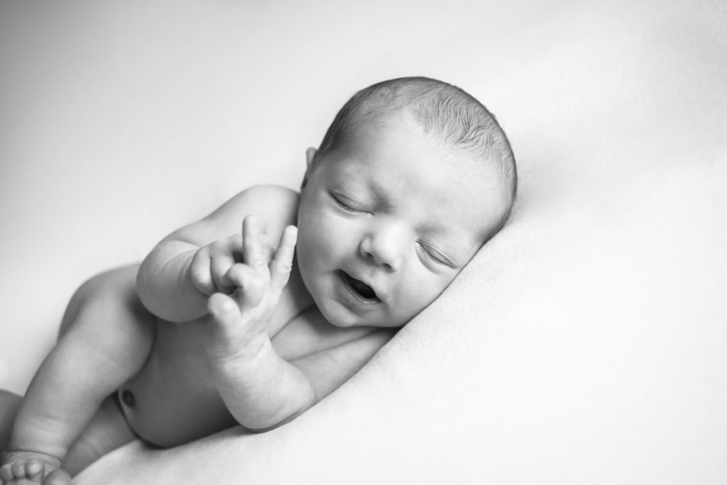 A caucasian newborn baby laying on it's side on a blanket. The baby is smiling and playing with their fingers. The photograph was taken at a photography studio near Johnson City, Tennesseee.