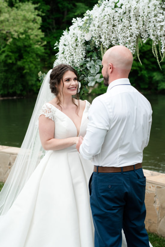 A wedding ceremony featuring a romantic white ball gown at riverbend Retreat. The bride is wearing makeup from Aesthetics by Hannah. The image was created by The Modern Heart, a wedding photographer in Erwin, Tennessee.